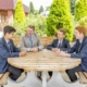 teacher chats to 3 students seated outside at table