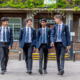 4 students walk towards camera in front of school gates