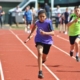 3 students race towards camera on rurnning track in relay race