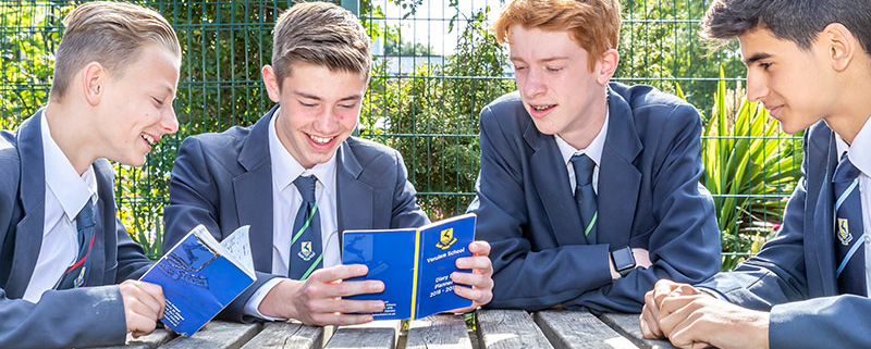 students sitting outside at table smiling at book